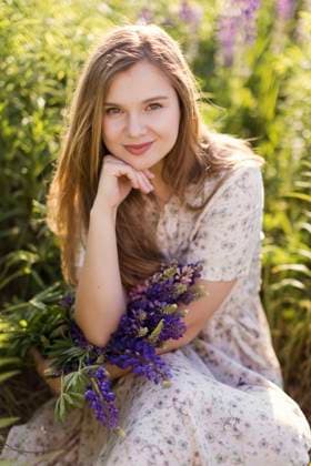 IMAGO Creative, Jahreszeit Frühling, Licht und Sonne Smiling woman with hand on chin and purple lupine flowers sitting in field model released, Symbolfoto, ONAF00563