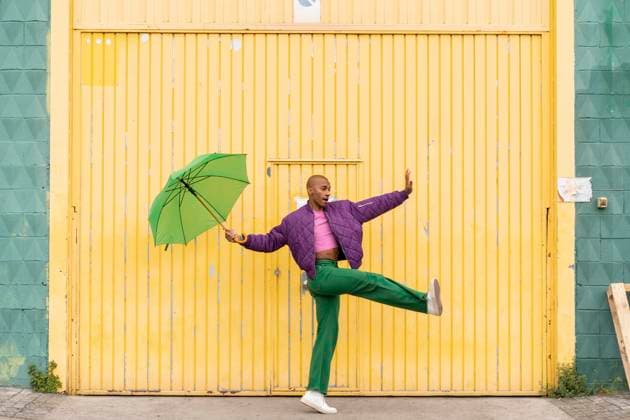 Non-binary person dancing with green umbrella in front of yellow shutter door model released, Symbolfoto, AFVF09352