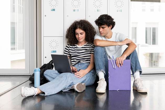 Young students using laptop sitting in front of locker at university model released, Symbolfoto, LMCF00632