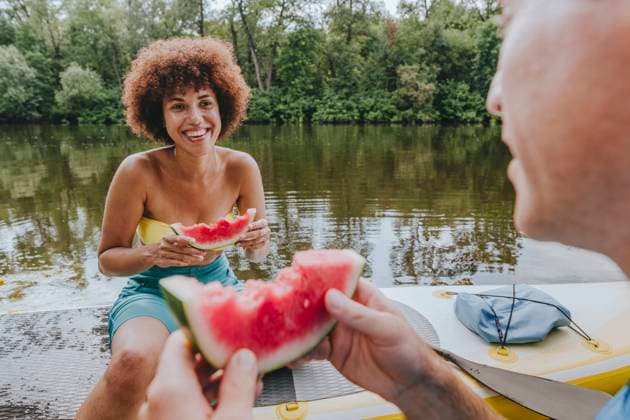 Smiling woman eating watermelon with friend on paddleboard in lake model released, Symbolfoto, YTF01035