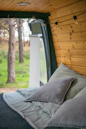 Tourist van with cozy bed pillows blanket near wooden planks wall ornament lights opened door with sun shade against blurred Andalusia trees Model Released LuisPina_ID16420_499229_019 Copyright: xLuisxPinax