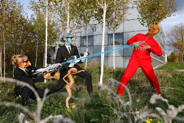 Aus dem FARBKÖRPER Kalender 2024 - Geek Art-Bodypainting und Transformaking: Men in Black Photoshooting mit Maria Skupin und Paul Skupin als außerirische MIB mit Neeble und Enrico Lein als Corn Face auf dem Expo-Gelände in Hannover. Ein Projekt des Fotografen Tschiponnique Skupin und des Bodypainters und Transformakers Enrico Lein