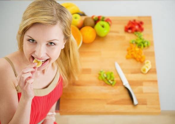 Portrait of happy young woman having a bite while cutting salad Copyright: Crestock 32190912