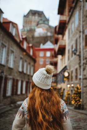 Woman with red hair in a white beanie walks down an old cobblestone street adorned with festive lights. Quebec, Canada Model Released CamilleGirard_ID13407_408461_002 Copyright: xCamillexGirardx