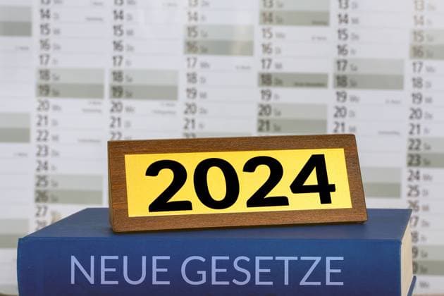 Symbolbild neue Gesetze 2024: Buch und Messingschild vor einem Kalender (Composing) *** Symbolic image of new 2024 laws Book and brass sign in front of a calendar Composing Copyright: xx