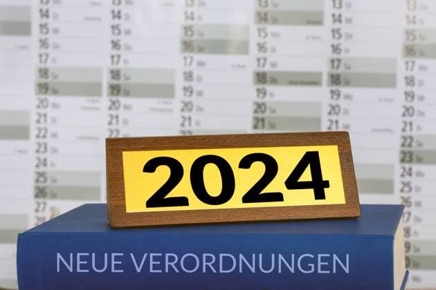 Symbolbild neue Verordnungen 2024: Buch und Messingschild vor einem Kalender (Composing) *** Symbolic image of new 2024 regulations Book and brass plate in front of a calendar Composing Copyright: xx