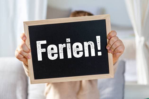 November 21, 2023: Chalkboard with vacation lettering. Child holding a sign with the text Ferien! PHOTOMONTAGE *** Kreidetafel mit Schriftzug Ferien. Kind hält ein Schild mit Text Ferien! FOTOMONTAGE