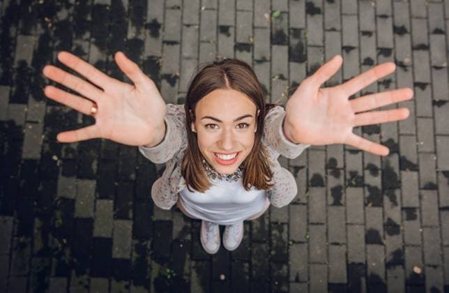IMAGO Creative, Lifestyle, Frühling in der Stadt Happy young woman raising her hands up outdoors Top view of happy young trendy woman raising her hands up over a gray street paving stone background Model Released DavidPereiras_ID17535_531542_016 Copyright: xDavidxPereirasx