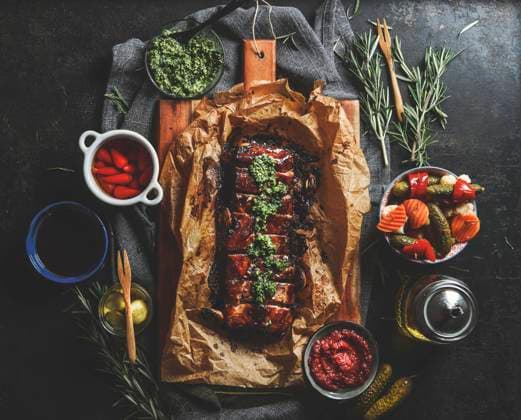 Roasted BBQ ribs with homemade pesto, pickled vegetables, sauces and rosemary on dark concrete kitchen table. Flavorful seasoned meat for dinner. Top view. Model Released Vicuschka_ID16617_505418_009 Copyright: xx