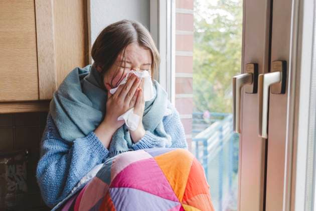 Sick girl blowing nose on tissue near window at home model released, Symbolfoto property released, IHF01816