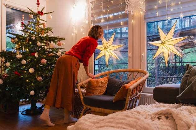 Woman standing near Christmas tree and looking through window at home model released, Symbolfoto property released, NDEF01394