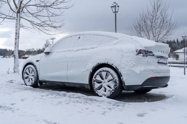 Ein zugeschneites Elektroauto der Marke Tesla, Tesla Model Y bedeckt mit Schnee