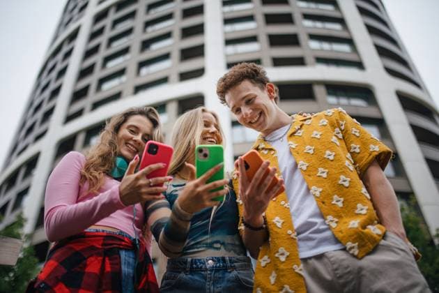 Generation z students hanging out together outdoors in the city. Generation z students hanging out together outdoors in the city. Young stylish zoomers are online, using smartphones, social media, taking selfies. Concept of power of friendship and social strength of gen Z. Low angle shot with copy space.