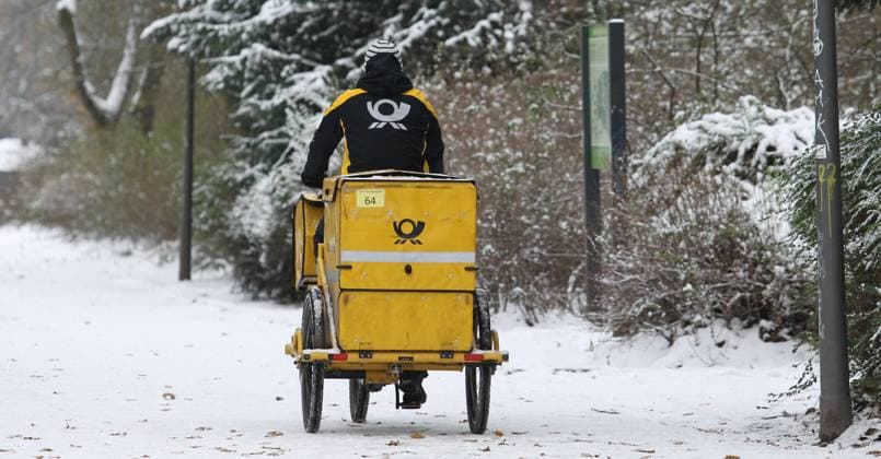 Ein Zusteller für Brief- und Verbundzustellung fährt mit seinem Fahrrad auf einem verschneiten Weg im Stadtpark Hamburg entlang. Winterhude Hamburg *** A deliverer for letter and parcel delivery rides his bike along a snowy path in Hamburgs Stadtpark Winterhude Hamburg