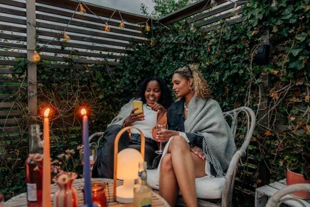 Smiling woman sharing smart phone with female friend sitting on chair in back yard Sweden, Stockholm, model released, property released Copyright: xMaskotx , MA105025 MA105025