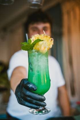 Blurred young male bartender showing a tropical green cocktail with a pineapple garnish at a bar Model Released AlvaroMontero_ID17423_529018_002 Copyright: xAlvaroxMonterox RECORD DATE NOT STATED