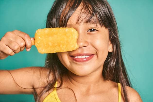 Happy ethnic girl child standing with popsicle near face against turquoise backdrop Cute crop Asian kid girl with long hair looking at camera while standing and covering eye with delicious yellow ice cream against turquoise background Model Released JoseDeJesusSaldana_ID16142_491319_034 Copyright: xJosexDexJesusxSaldanax