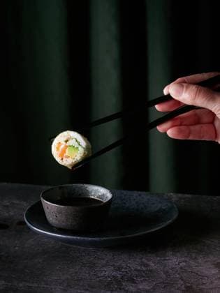 Creative Highlights Symbolbilder Sushi roll held by anonymous person using chopsticks with a droplet of sauce ready to fall in bowl placed on table against green curtains Model Released AnaLopez_ID17504_530934_005 Copyright: xAnaxLopezx RECORD DATE NOT STATED