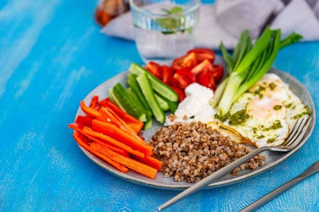 A nutritious breakfast setup showcasing sliced raw vegetables, feta cheese, buckwheat, and fried eggs with pesto on a blue background. Model Released AnnaBogush_ID18101_544315_008 Copyright: xAnnaxBogushx