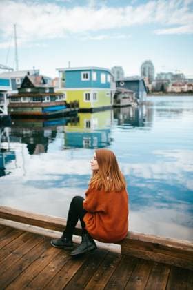 Creative Highlights Symbolbilder A contemplative redhead woman sits on a wooden dock, gazing at the serene waters surrounded by vibrant floating homes in Victoria, Vancouver Island, British Columbia. Model Released CamilleGirard_ID17696_535219_001 Copyright: xCamillexGirardx