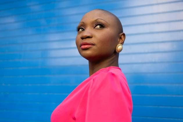 Creative Highlights Symbolbilder Portrait of young African American female with shaved head in pink clothes and makeup looking away while standing near blue striped wall on city street Model Released DavidMunoz_ID17368_528133_006 Copyright: xDavidxMunozx