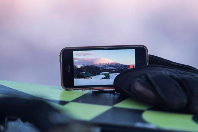 MR_ID16589_15318_JuanAizpuru.jpg Closeup of smartphone with bag on table photographing beautiful snowcapped mountain with cars and houses on snow covered landscape against sky at Japan Model Released JuanAizpuru_ID16589_503957_003 Copyright: xJuanxAizpurux