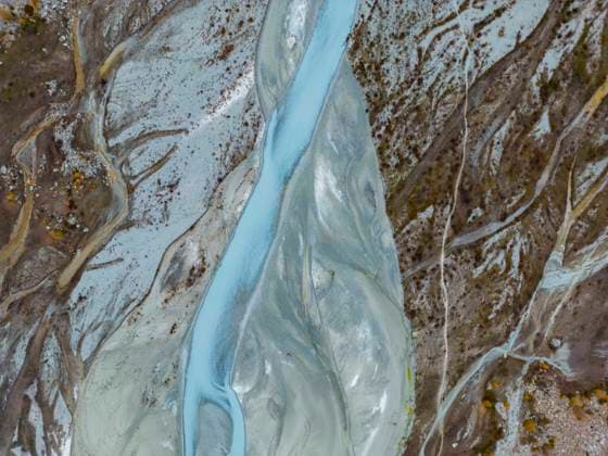 This aerial image captures the intricate path of a glacial river as it snakes through a rugged, mud-streaked landscape, highlighting the striking contrasts of natural earth tones. Model Released JuanAizpuru_ID17815_537710_008 Copyright: xJuanxAizpurux