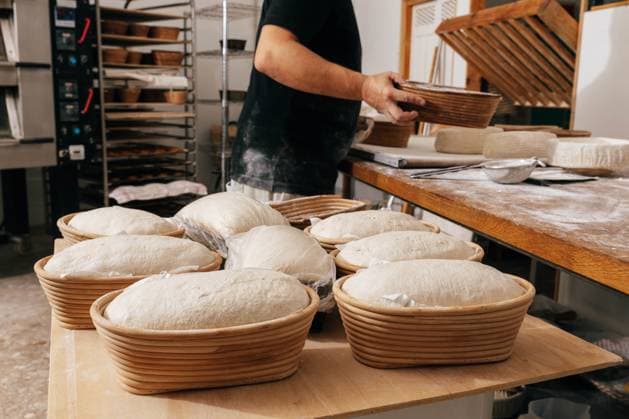 Side view of focused anonymous male professional baker covering uncooked sourdough bread in molds with plastic on wooden table in kitchen at bakehouse Model Released SergioVictorVega_ID16859_514996_013 Copyright: xSergioxVictorxVegax