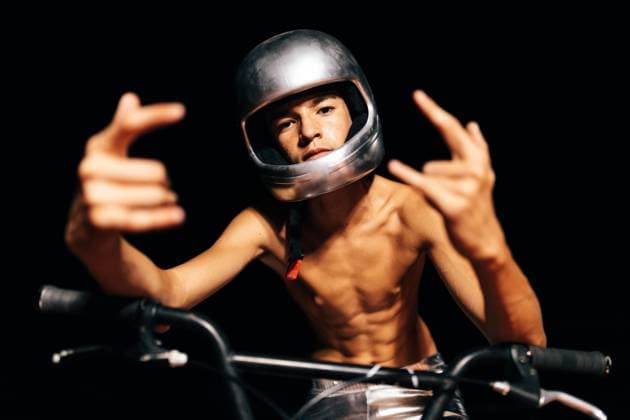 Creative Highlights Symbolbilder Unrecognizable young shirtless man sitting on bicycle in lights and showing devil horns gesture Anonymous shirtless young stuntman in helmet looking at camera while sitting on bicycle seat with fingers displaying rock and role gesture with elbows on handlebar in illuminated light against dark background Model Released SergioVictorVega_ID17382_528490_028 Copyright: xSergioxVictorxVegax