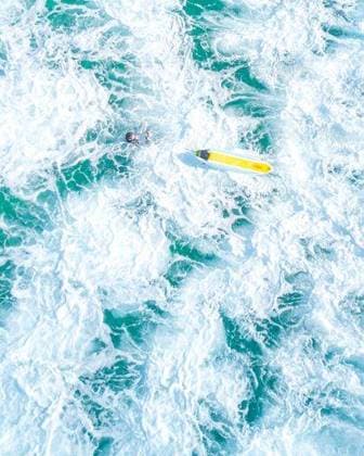 An overhead vertical shot of a surfer with a yellow surfboard in a blue sea 35571 RECORD DATE NOT STATED