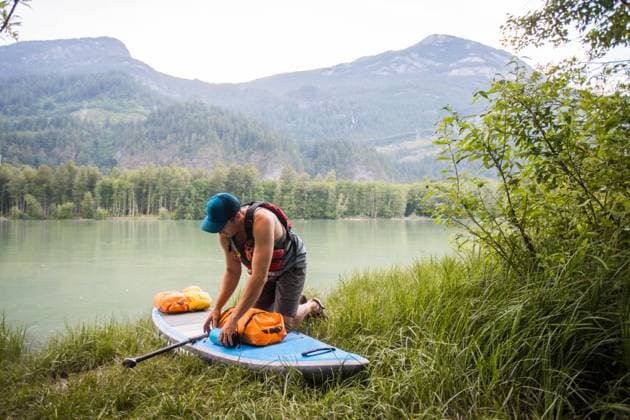 SUP Paddle boarder secures dry bags and gear before paddling. Squamish, British Columbia, Canada CR_JDIP231218-1200097-01 ,model released, Symbolfoto