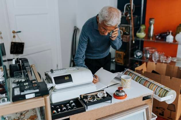 Elderly male owner writing in diary while talking on mobile phone in store Sweden, Gothenburg, model released, property released Copyright: xMaskotx , MA106135 MA106135