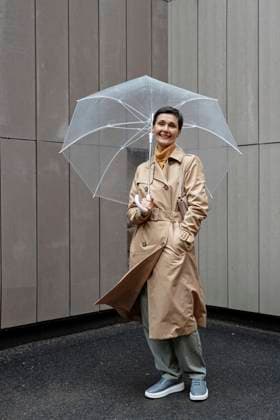 Happy woman in beige raincoat holding umbrella while walking outside, looking at camera model released, Symbolfoto, KPEF00393