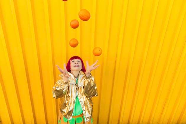 Creative Highlights Symbolbilder Happy senior woman juggling oranges in front of yellow wall model released, Symbolfoto, LLUF01136