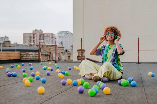 Creative Highlights Symbolbilder Smiling young woman listening to music sitting cross-legged amidst colorful balls on terrace model released, Symbolfoto property released, YTF01417