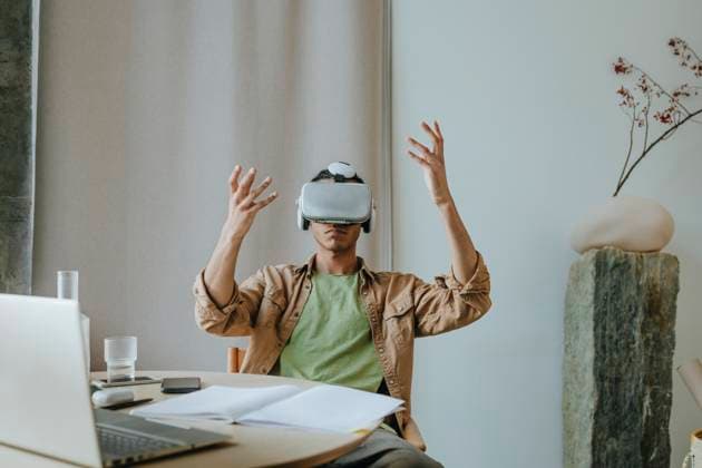 Creative Highlights Symbolbilder Young man wearing VR headset sitting with arms raised at table model released, Symbolfoto property released, YTF01500