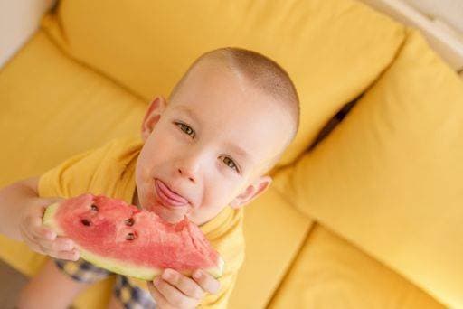 A closeup of a male child eating watermelon on a yellow couch 623215 ,model released, Symbolfoto RECORD DATE NOT STATED