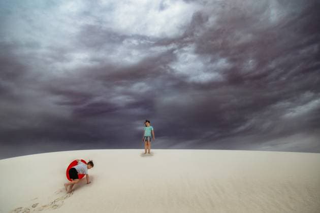 Creative Highlights Symbolbilder Two young kids climbing on sand dunes with stormy sky Alamogordo, New Mexico, United States CR_KRRY231229-1313856-01 ,model released, Symbolfoto