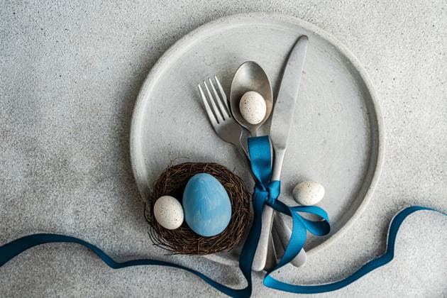 Top view of minimalist yet stylish Easter table setting, with cutlery tied together with blue ribbon on concrete plate, with a small nest with decorative Easter eggs, placed on gray table Model Released AnnaBogush_ID18583_554018_021 Copyright: xAnnaxBogushx