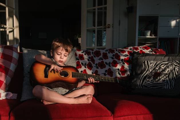 Creative Highlights Symbolbilder Preschool boy sits on couch and plays with child guitar in sunlight Reading, Pennsylvania, United States CR_LIDE240105-1314634-01 ,model released, Symbolfoto