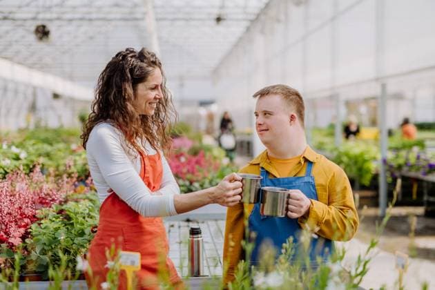 IMAGO Creative: Garten, Anbau im Gewächshaus Woman florist with her young colleague with Down syndrome having tea break in garden centre. A woman florist with her young colleague with Down syndrome having tea break in garden centre. model released Copyright: xx Garden_Centre_Down_Syndrome_Peter_2022_233
