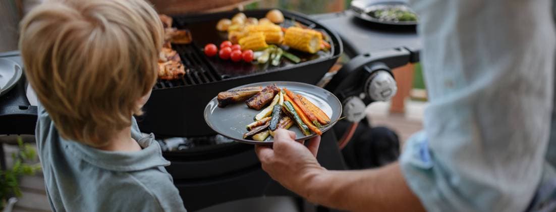 Father putting grilled meat and vegetable on plate to his son during family summer garden party. A father putting grilled meat and vegetable on plate to his son during family summer garden party. model released Copyright: xx HHH FAMILY GRILL BODOVCI 2022 HHH 153