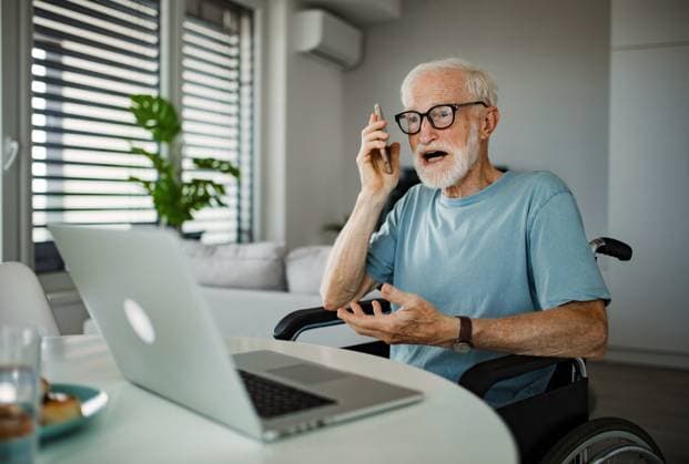 Senior man in a wheelchair working during retirement. Senior man in a wheelchair working from home during retirement. Elderly man using digital technologies, working on a laptop and making phone call at home. Concept of seniors and digital skills. Senior calling customer service to complain. model released Copyright: xx HHH SENIOR CITY LIFESTYLE 2023 HHH 056.jpeg