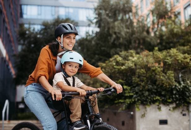 Mother carring her son on a child bike carrier, seat, both wearing helmets. Mom commuting with a young child through the city on a bicycle. Mother carring her son on a secure child bike carrier or seat, both wearing helmets. Mom commuting with a young child through the city on a bicycle. model released Copyright: xx HHH WOMAN POWER DAY IN LIFE 2023 HHH 196