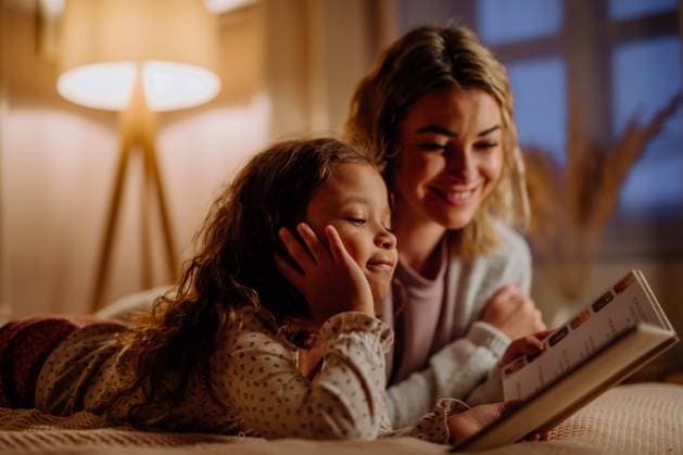 Happy mother with her little daughter lying on bed and reading book in evening at home. A happy mother with her little daughter lying on bed and reading book in evening at home. model released Copyright: xx Mother_and_Daughter_at_Home_2021_259