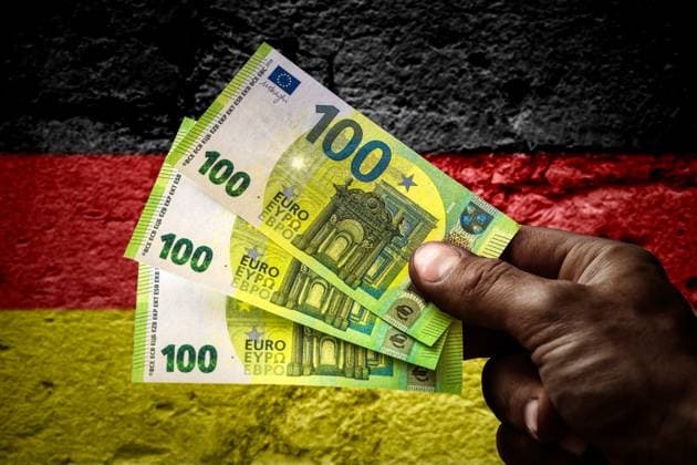 January 18, 2024: Hand of an asylum seeker holding several hundred euro banknotes in front of a Germany flag. Symbolic image of money and benefits in kind for refugees PHOTOMONTAGE *** Hand von einem Asylbewerber hält mehrere hundert Euro Geldscheine vor einer Deutschland Flagge. Symbolbild Geld und Sachleistungen für Geflüchtete FOTOMONTAGE