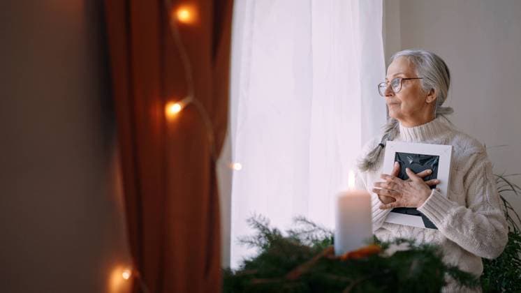 Nostalgic senior woman holding picture frame, standing by window at home. A nostalgic senior woman holding picture frame, standing by window at home. model released Copyright: xx Untitled_1.31.2