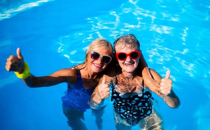 High angle view of cheerful senior women in swimming pool outdoors in backyard. High angle view of cheerful senior women in swimming pool outdoors in backyard, looking at camera. model released Copyright: xx Summer_Splash_Seniors_2020_315
