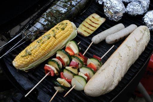 A high angle shot of seasoned vegetables on skewers, sausages, bread and stuffed fish cooking on grill 2386262