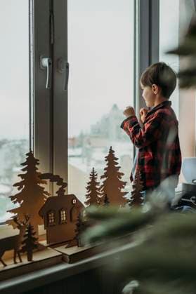 Boy standing near Christmas decoration and looking through window at home model released, Symbolfoto property released, ANAF02618